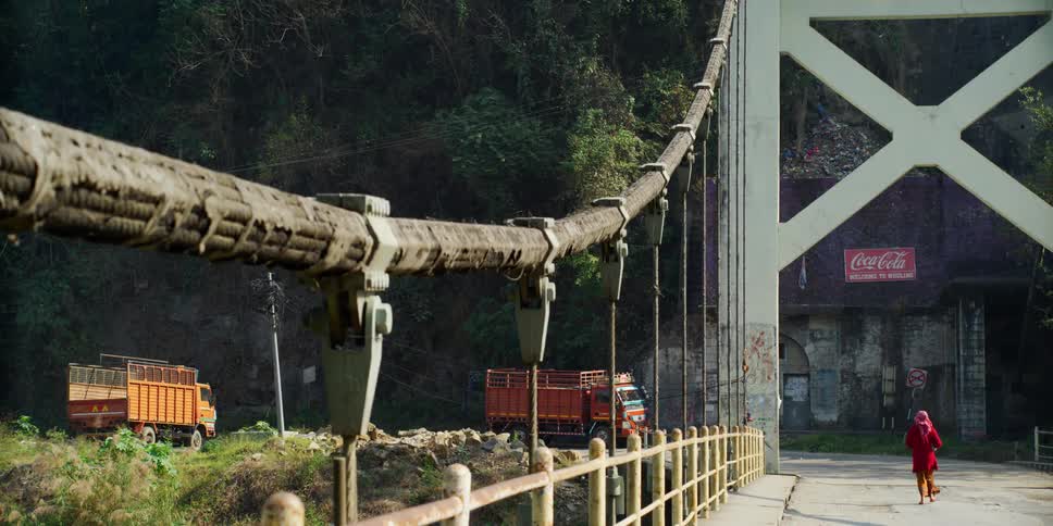 A woman crosses a bridge walking towards a parked truck near the mountains