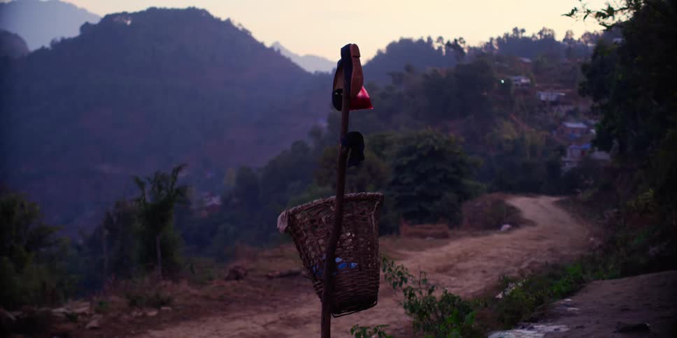 Basket and shoes hanging from a wooden pole on a dirt road near a village on the mountains