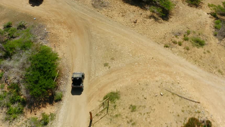 Two vehicles are driving on a dirt road in a rural area