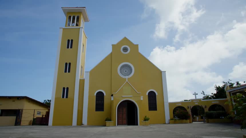 A tower and church with an arched door and windows are painted bright yellow