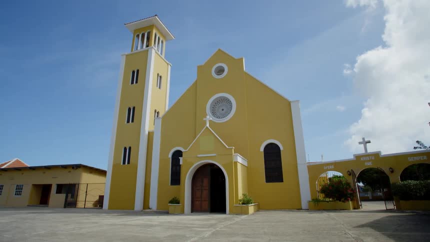 A church with the front door open and windows with the sky and clouds in the background