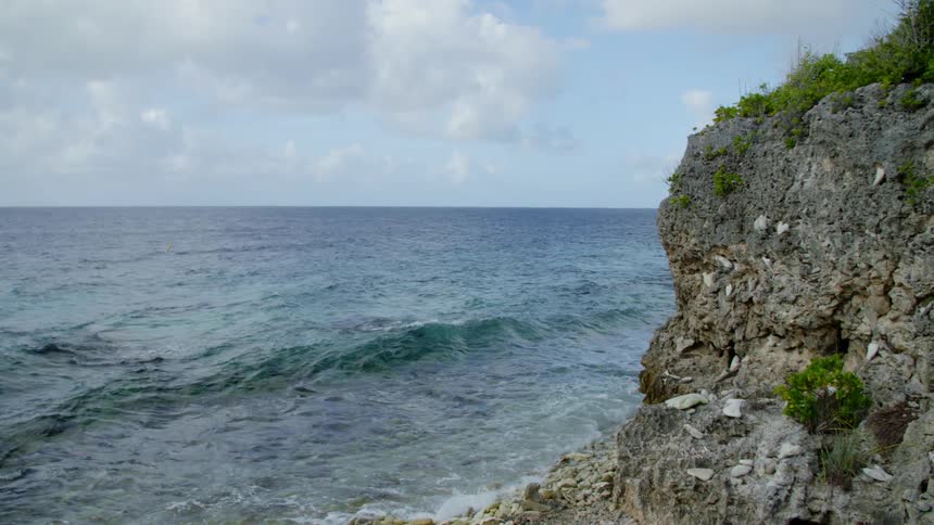 Ocean waves wash towards a coastline with tall rocky cliffs