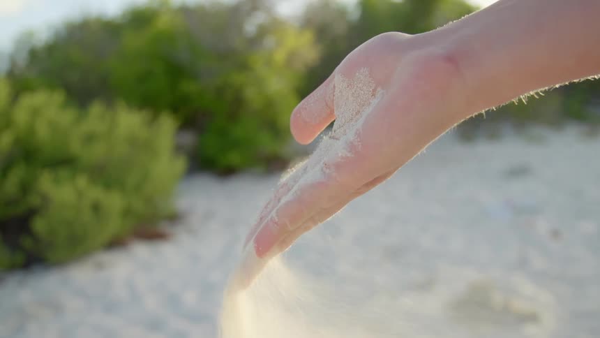 A person opens up their hand that is filled with sand and lets the wind it out