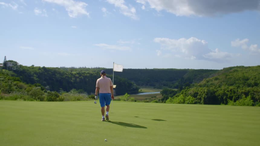 A golfer approaches a flag on a golfing green atop a canyon and pulls the flag up from the grass