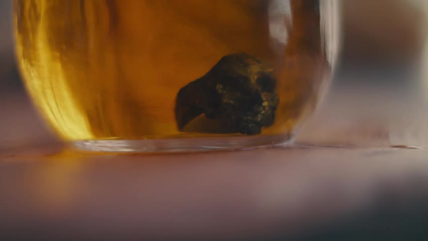 A ring shaped like a skull being placed in a yellow liquid in a glass on a table