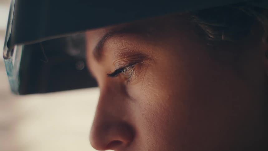 A woman slowly raises her safety goggles from over her eyes allowing light to shine onto her face