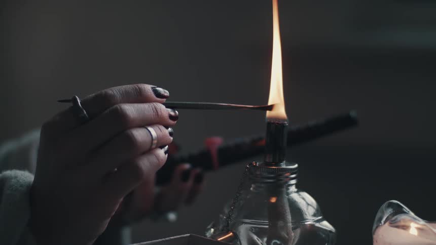 Woman uses an oil lamp to heat a tool to melt a wax seal