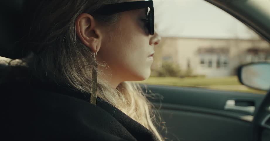 Woman wearing sunglasses drives a car on the streets of a small town