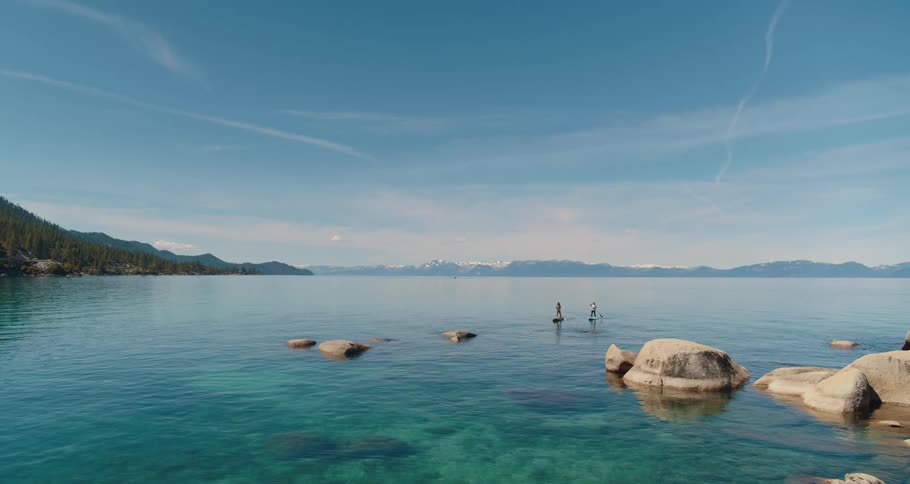 Two people paddle board on a lake on a summer day