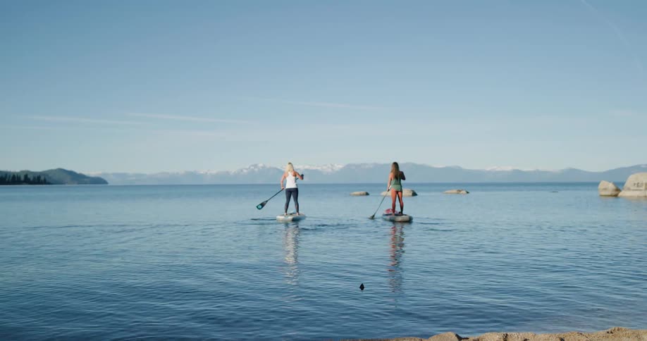 Two women paddle board across a large lake