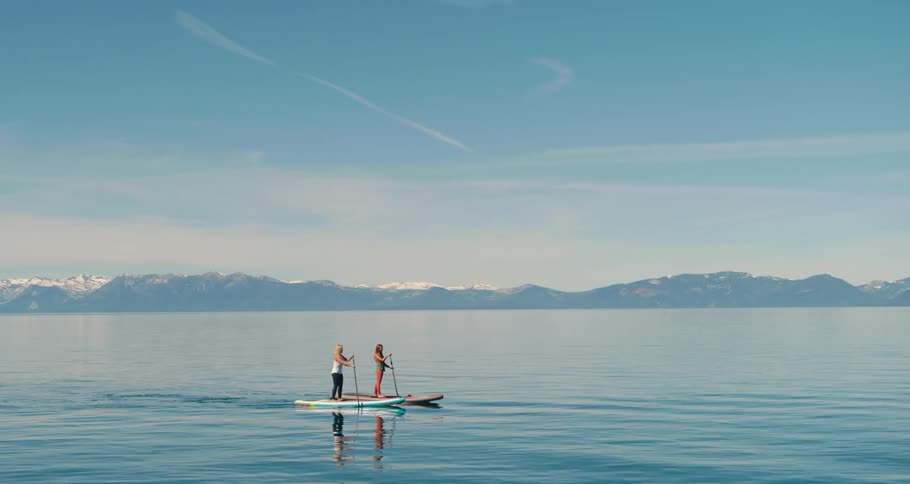 Two fit woman paddle boarding on a lake in the mountains
