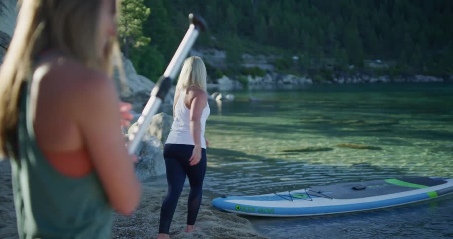 A woman gets off a paddle board and brings it to the surface at a lake in a forest