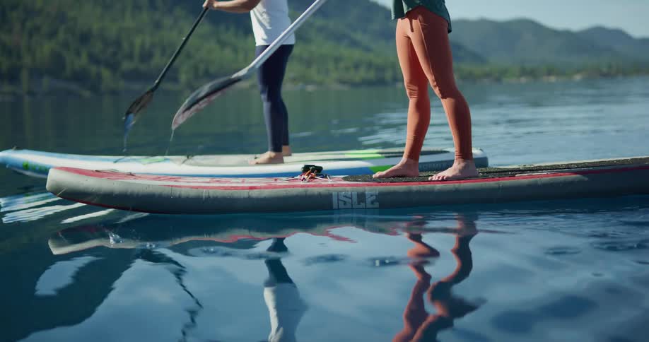 Two women paddle board on a lake on a sunny summer day
