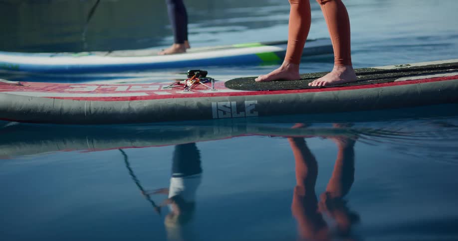 Young fit women paddle boarding on the surface of a lake next to the mountains