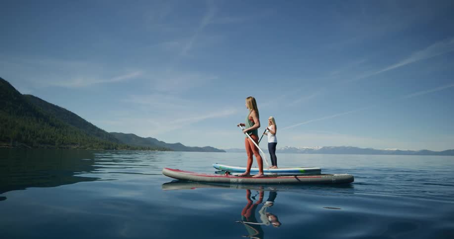 Two women move forward on sup boards in a tranquil lake