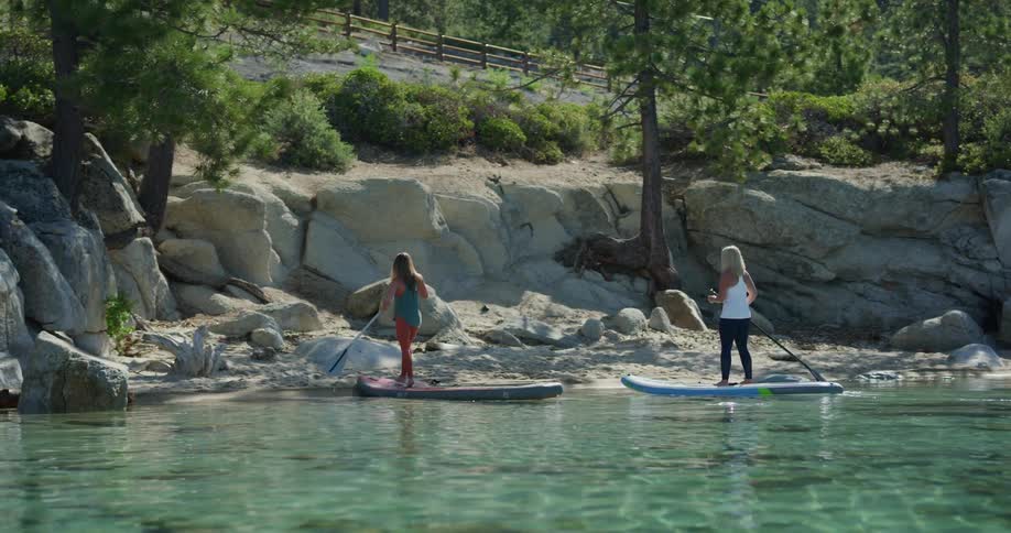 Two women paddle boarding reach the shore and step off their boards