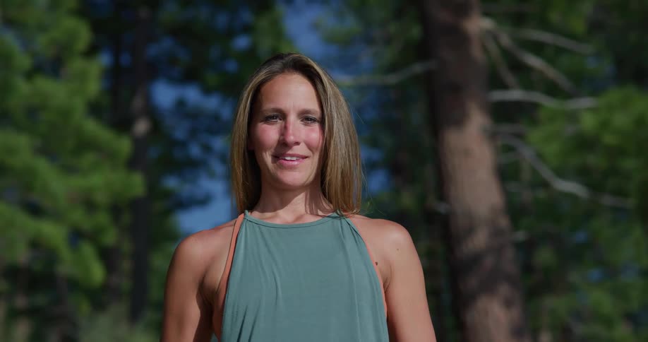 A woman is smiling outdoors in a forest