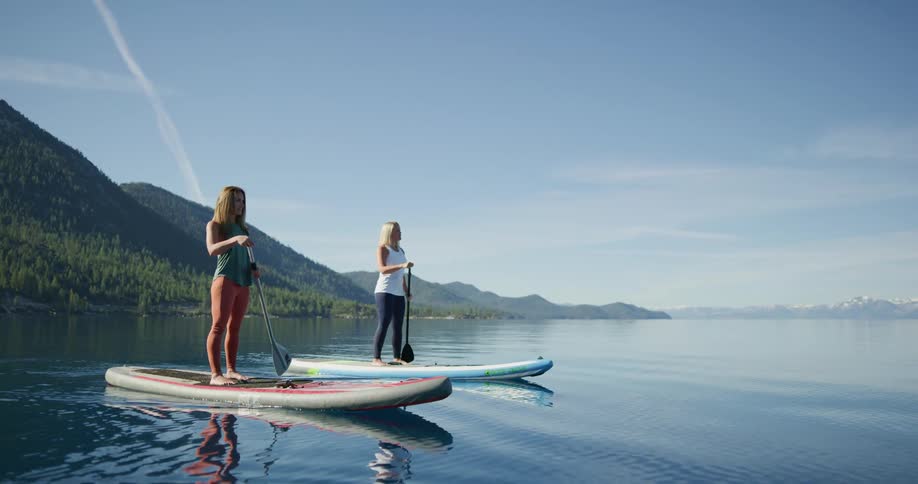 Two women move forward on sup boards in a tranquil lake