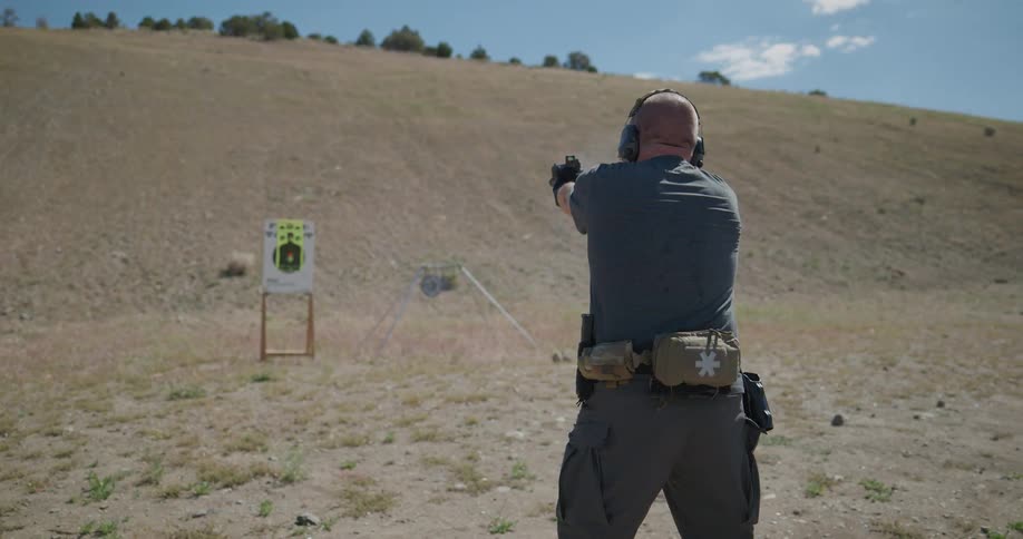 A police office removes his handgun from its holster and fires at a paper target staged at the bottom of a steep hill