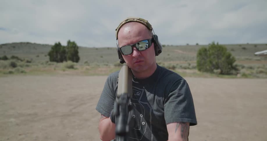 A caucasian male standing and pointing a rifle