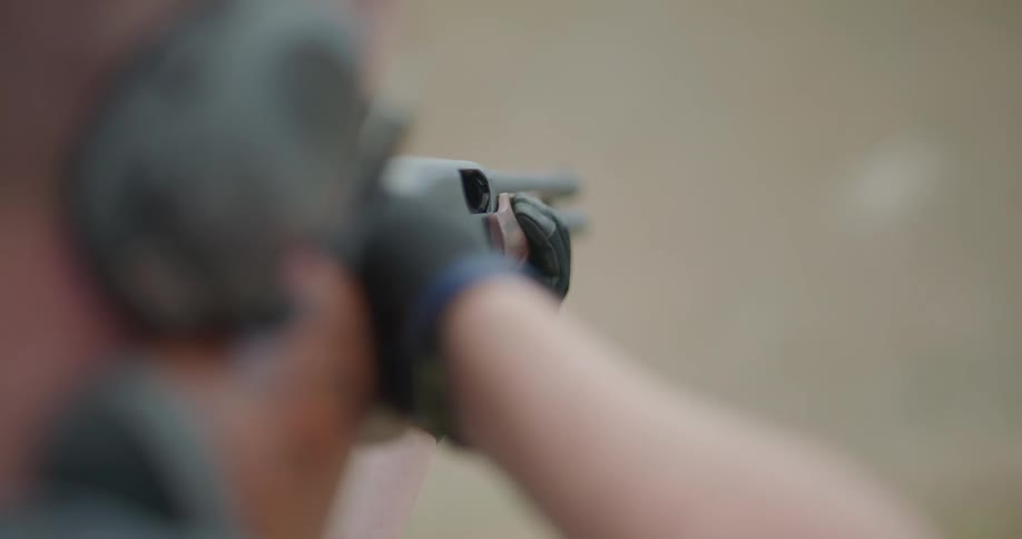 A man with glasses earmuffs and gloves aiming and shooting a shotgun