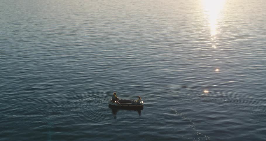 Two men drift across water in inflatable boat while sun reflects of rippling water