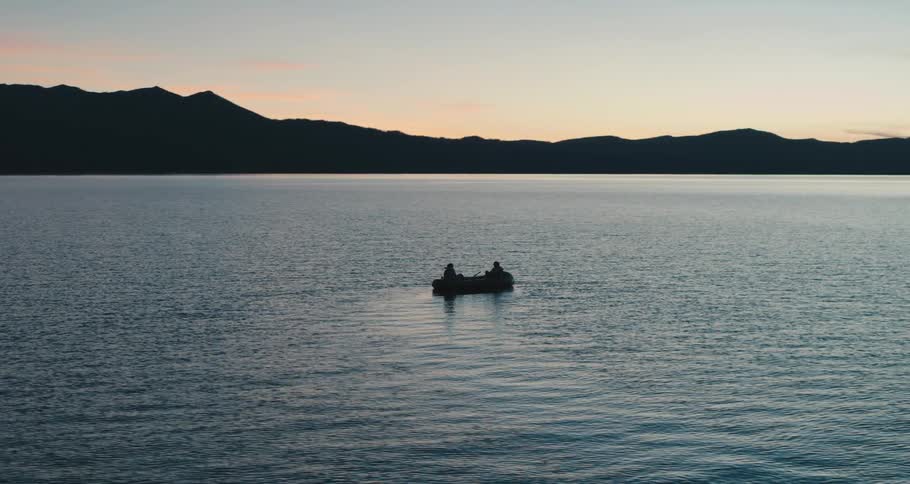 Couple of people on a row boat in the middle of a lake near the mountains at sunset