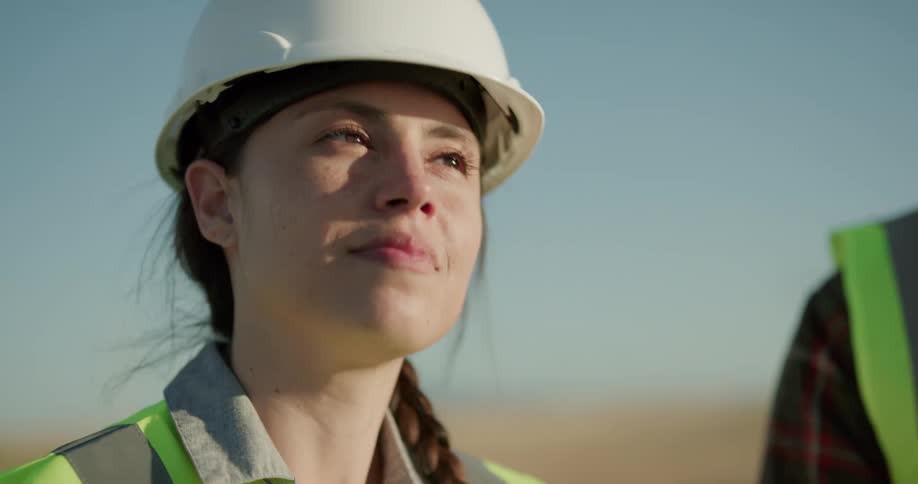 Female supervisor wearing a white hard hat and green vest on a construction site