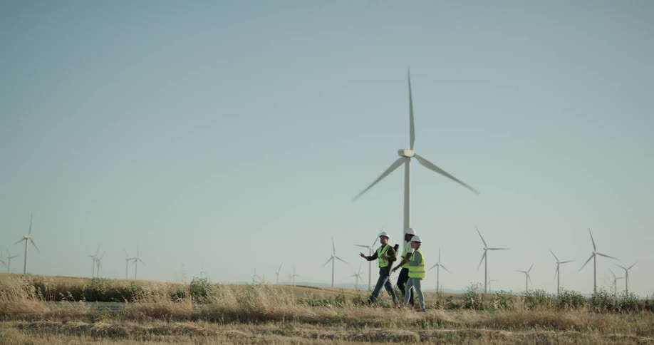 Wind energy engineers walk and do analysis on wind farm with wind turbines in the background
