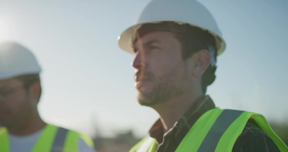 Two men in hard hats use a tablet and look at the sky as they use a controller