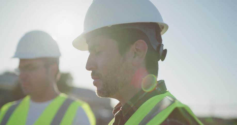 Two constructions workers are outdoors at dusk