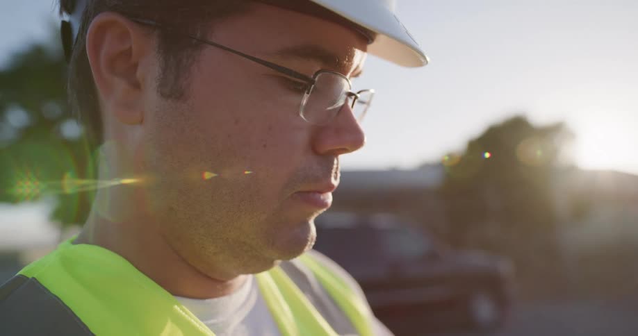 A man in a brightly colored vest and hard hat stands at a construction site