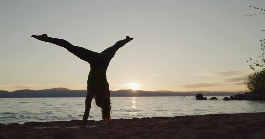 Silhouette of a woman practicing yoga on the shore of a lake in the mountains at sunset