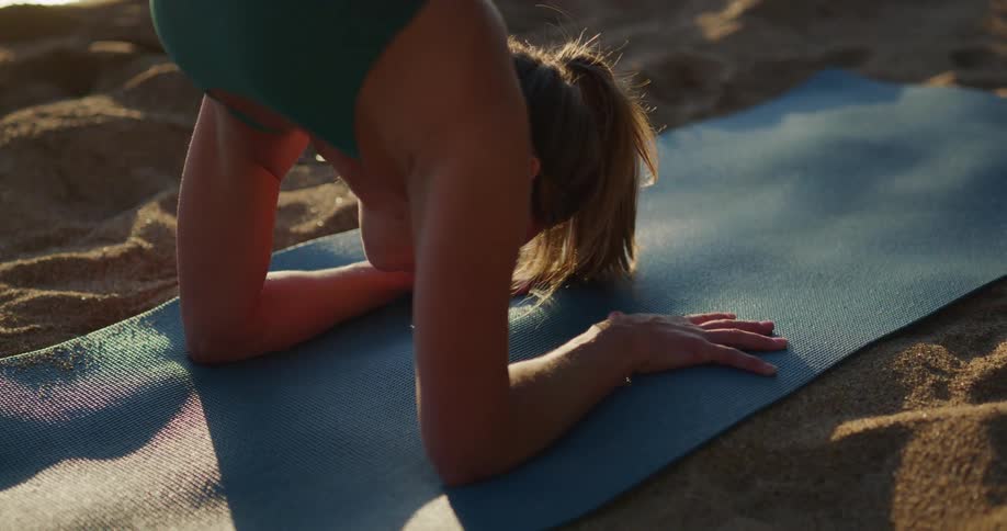 A woman does a hand stand on her yoga mat near the water