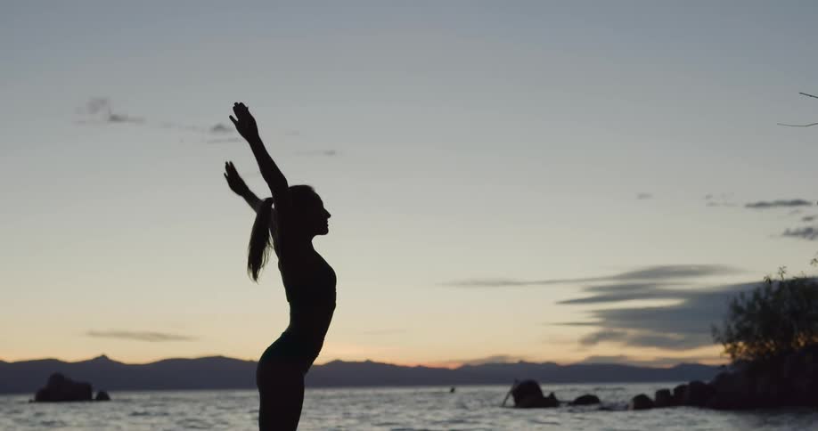 A woman is stretching on a beach at dusk