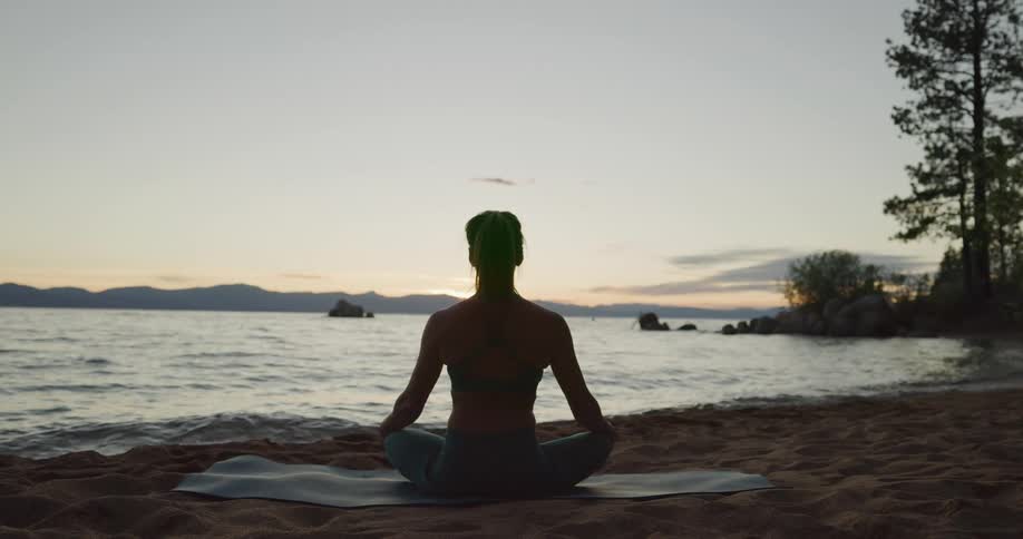 A woman is sitting on a yoga mat on the beach