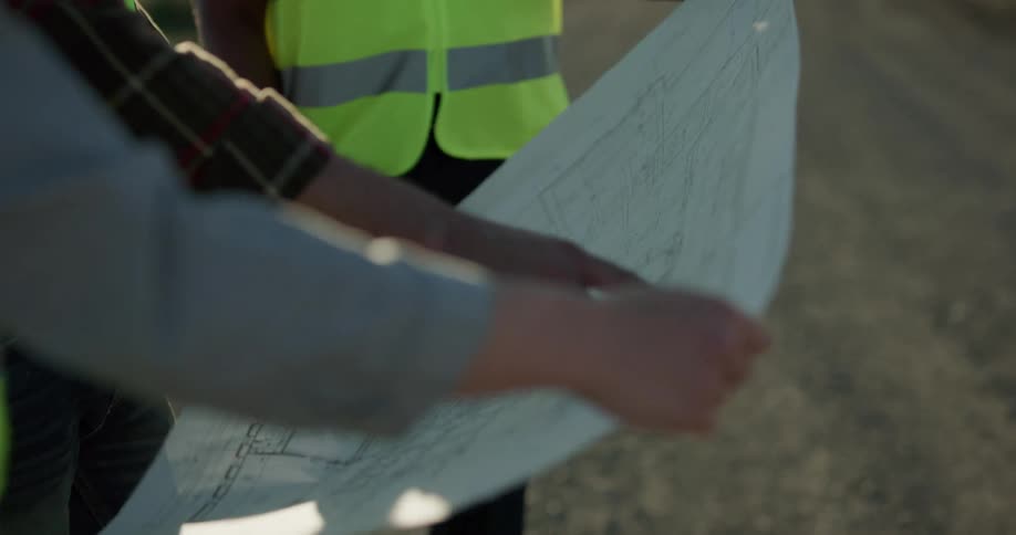 Two men and a woman with hard hats and vests looking at a paper with the sky and wind turbines in the background