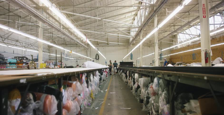A factory with workers and rows of rolled up material and rugs