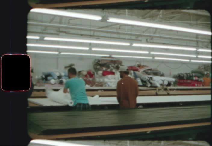 Workers wear face masks while working at long tables under florescent lights