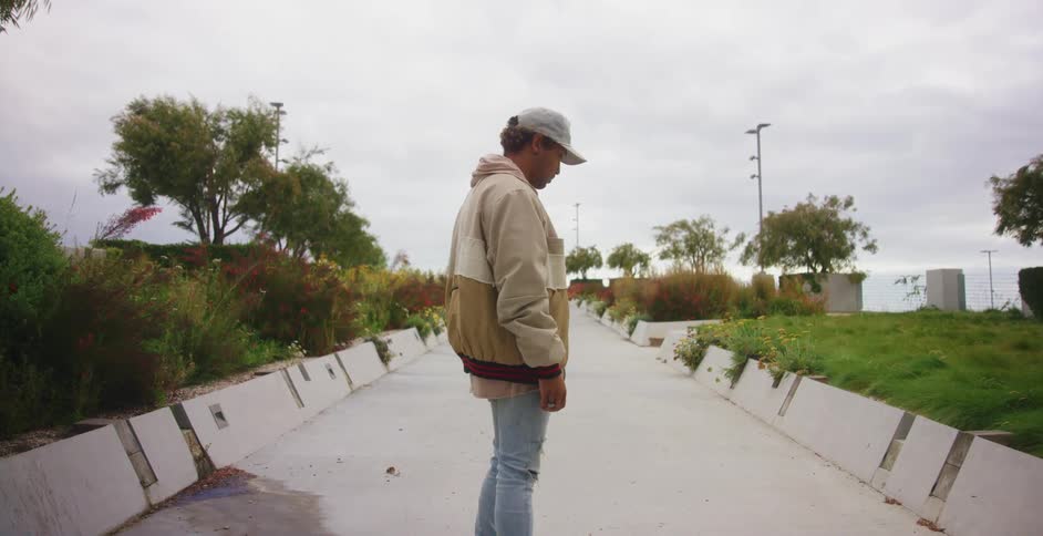 A man stands on a walkway with his head lowed in thought for a moment before raising his head to look around him