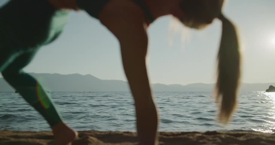 Woman practices yoga on the sand of a lake shoreline in the mountains