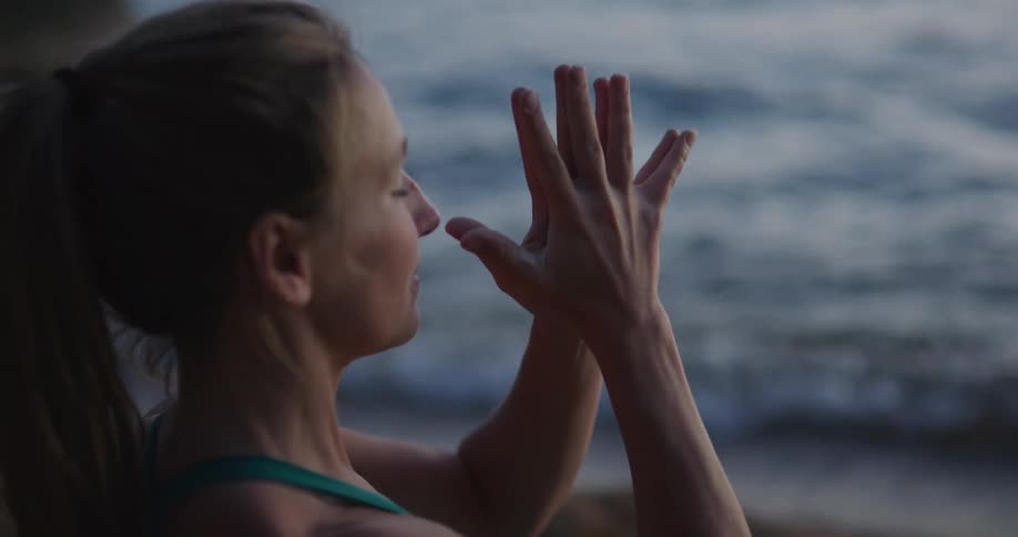 Side view of a woman practicing yoga at the coast next to the sea at dusk