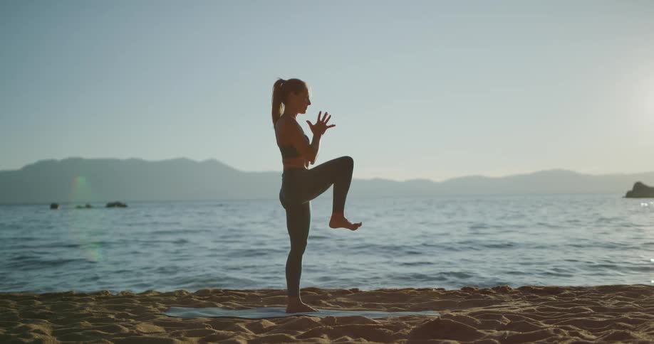 A woman practices yoga on the shore of a large lake in the evening