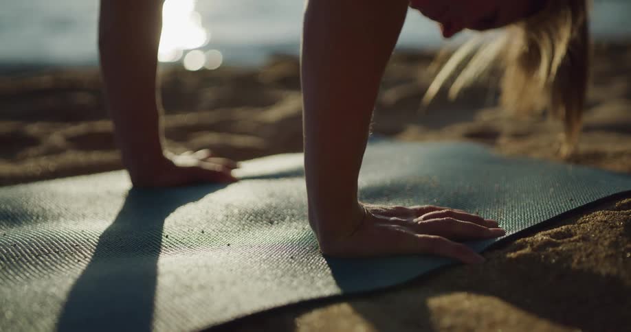 Woman practices yoga over a mat in the sands of a lake shore in the mountain
