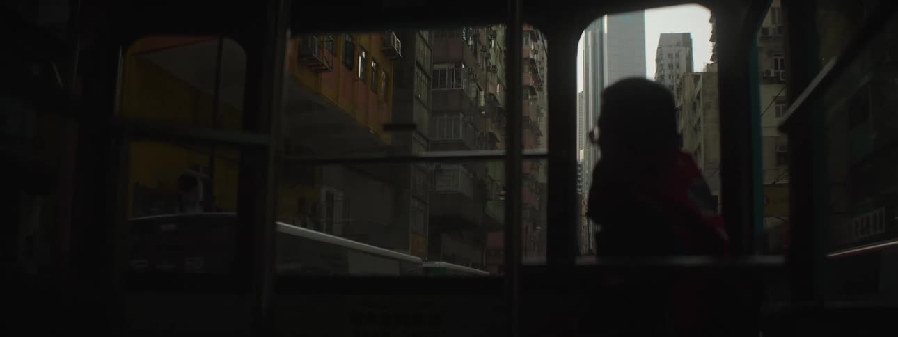 A man looks out the window of a bus as it drives through a narrow street lined with apartment buildings near downtown