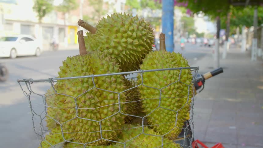 Wire basket on the back of a motorcycle parked on the sidewalk of a busy city street filled with green durians