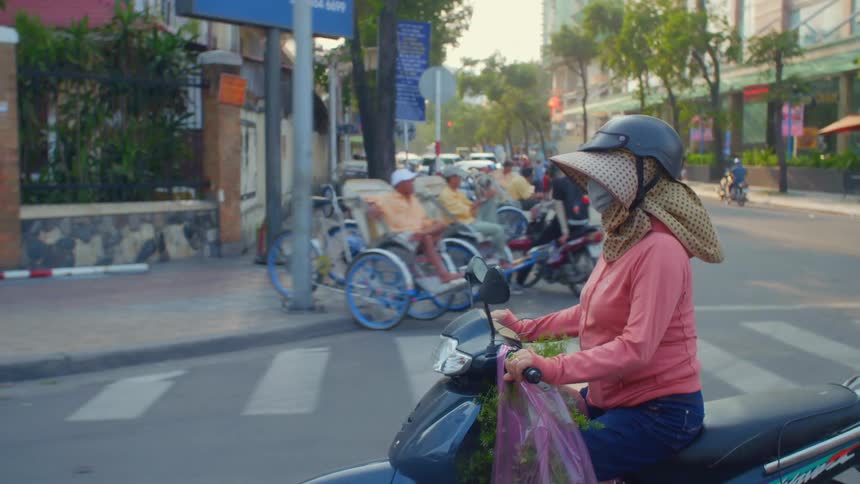 Woman in face mask and hat riding motor scooter down neighborhood street
