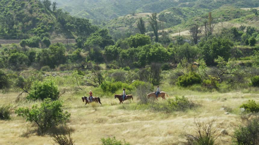 People riding horses on a dirt road through the hills at day
