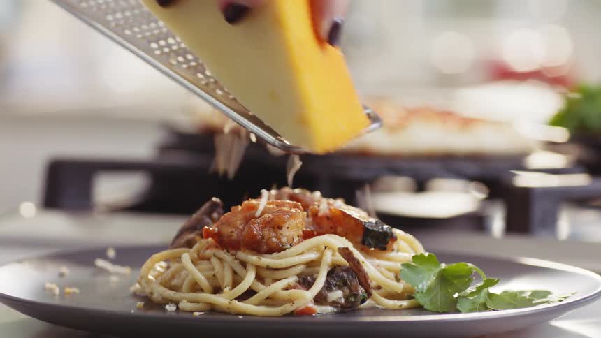 Parmesan cheese being grated over plated pasta