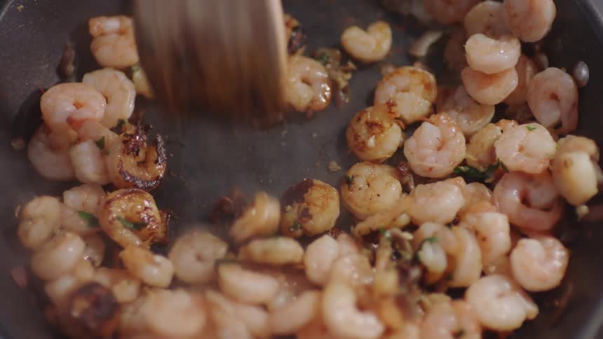 A person is cooking shrimp in a frying pan